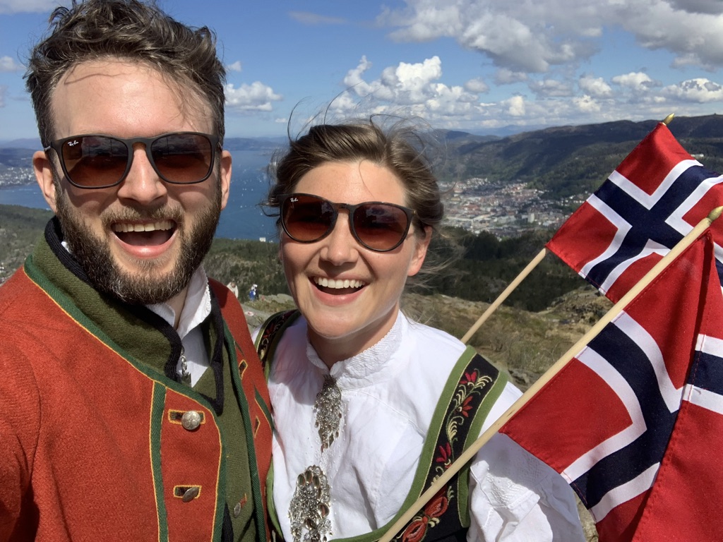 Kristina og Kenneth i bunad på fjellet med flagg, Bergen i bakgrunnen